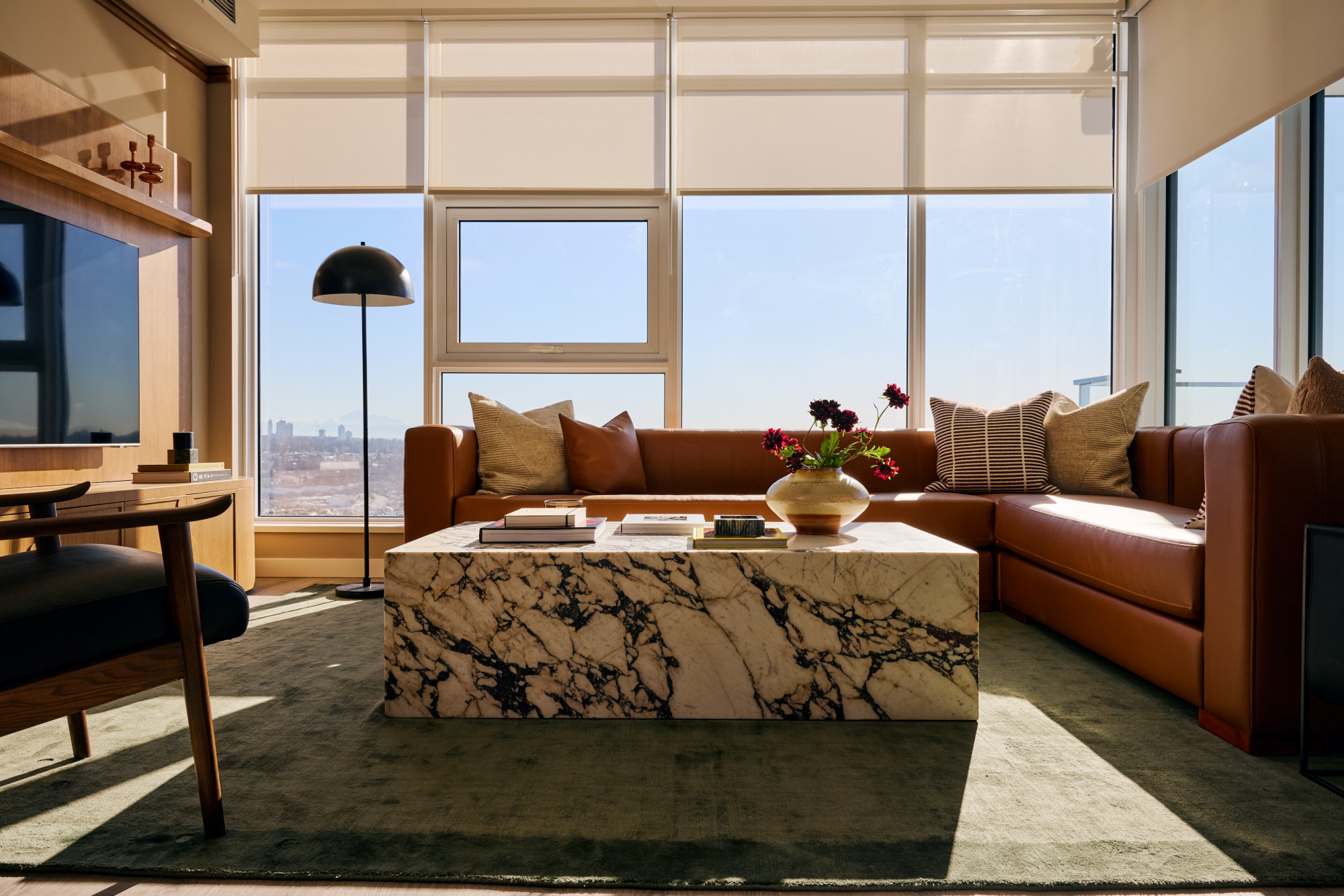 Living room with a custom marble coffee table and a caramel leather sectional. A black mushroom shaped floor lamp in the corner.