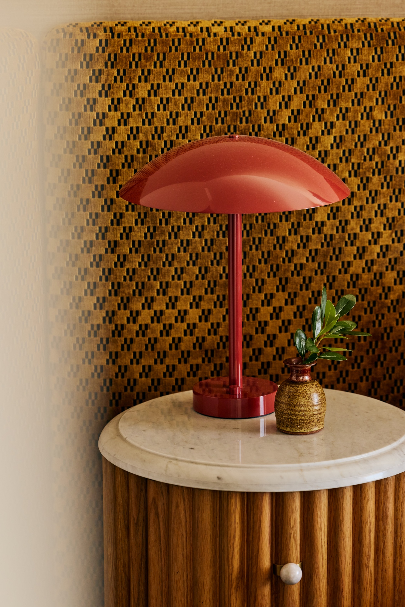 Vignette of nightstand with a red mushroom lamp and marble and wood nightstand.